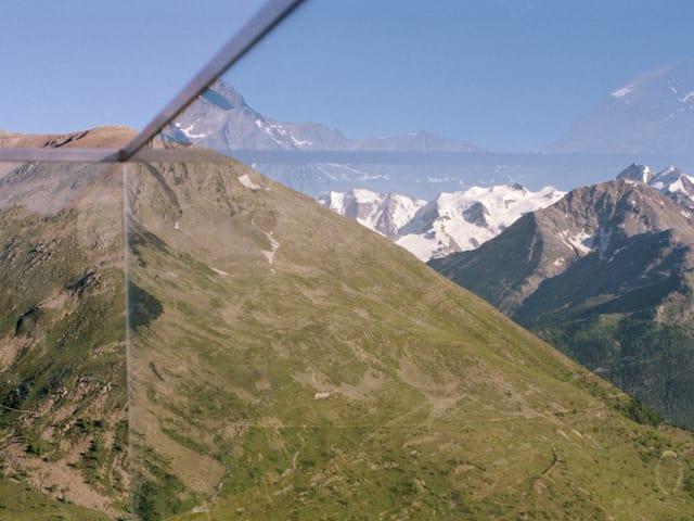 Eine Berglandschaft, davor ein Absperrglas, das mit Metallstreben in vier Teile geteilt wird. Eine Berglandschaft, davor ein Absperrglas, das mit Metallstreben in vier Teile geteilt wird.