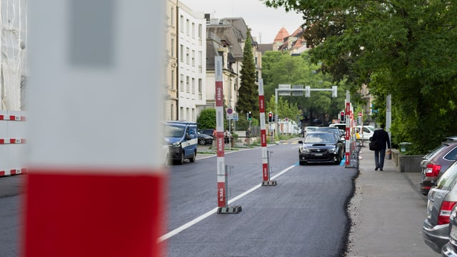 Frisch ausgebrachter Asphalt auf einer Strasse, Bauabschrankungen, parkierte Autos Frisch ausgebrachter Asphalt auf einer Strasse, Bauabschrankungen, parkierte Autos