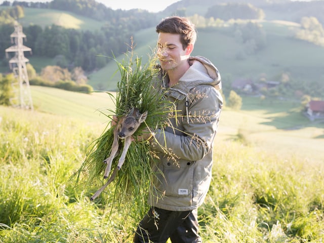 Junger Mann auf einer Wiese mit einem Rehkitz in den Armen. Junger Mann auf einer Wiese mit einem Rehkitz in den Armen.
