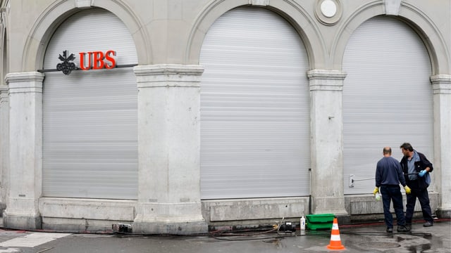 Zwei Arbeiter vor einer geschlossenen UBS-Filiale. Zwei Arbeiter vor einer geschlossenen UBS-Filiale.