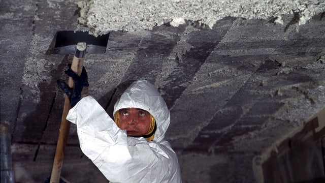 Arbeiter mit Schutzanzug kratzt Asbest von einer Decke. Arbeiter mit Schutzanzug kratzt Asbest von einer Decke.