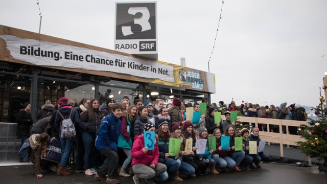 Die Glasbox der Spendenaktion Jeder Rappen zählt in Luzern. Im Vordergrund eine Schulklasse. Die Glasbox der Spendenaktion Jeder Rappen zählt in Luzern. Im Vordergrund eine Schulklasse.