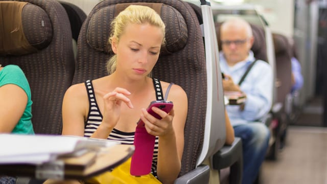Eine Frau sitzt im Zug und tippt auf ihrem Handy. Eine Frau sitzt im Zug und tippt auf ihrem Handy.