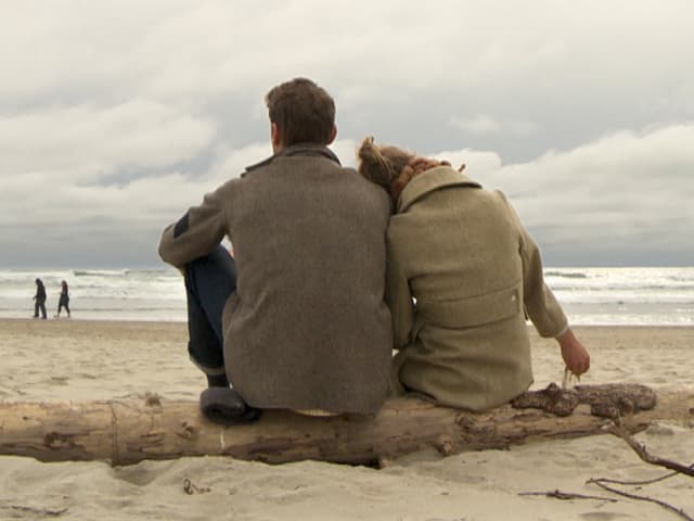 Von hinten photographiertes Liebespaar, das auf einem Baumstamm am Strand sitzt. Von hinten photographiertes Liebespaar, das auf einem Baumstamm am Strand sitzt.