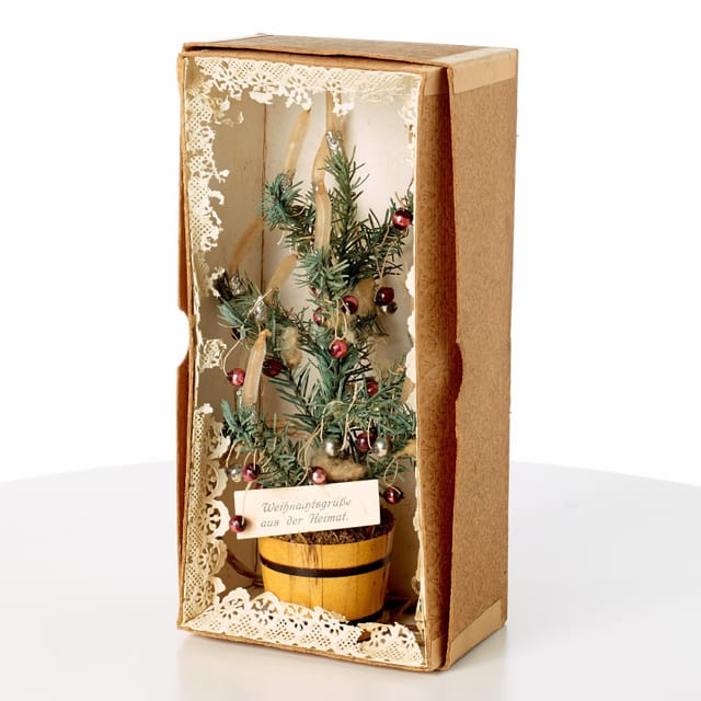 Ein Mini-Weihnachtsbaum in einer kleinen Kartonbox. Auf einer Etikette steht «Weihnachtsgrüsse aus der Heimat». Ein Mini-Weihnachtsbaum in einer kleinen Kartonbox. Auf einer Etikette steht «Weihnachtsgrüsse aus der Heimat».