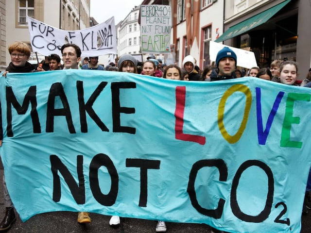 Demonstrierende halten ein Plakat, worauf steht; "Make love, not CO2". Demonstrierende halten ein Plakat, worauf steht; "Make love, not CO2".