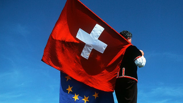 Mann in Sennentracht schultert eine Schweizer und eine EU-Fahne vor blauem Himmel. Mann in Sennentracht schultert eine Schweizer und eine EU-Fahne vor blauem Himmel.