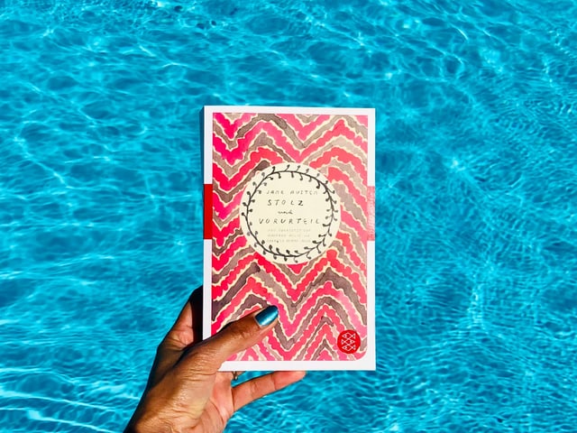 Der Roman «Stolz und Vorurteil» von Jane Austen vor leuchtend blauem Wasser Der Roman «Stolz und Vorurteil» von Jane Austen vor leuchtend blauem Wasser