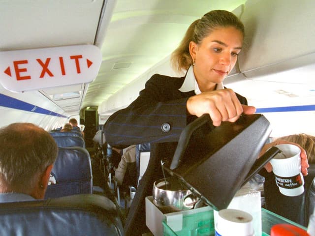 Flight Attendant serviert Kaffee während eines Fluges. Sie ist sehr konzentriert bei der Arbeit. Flight Attendant serviert Kaffee während eines Fluges. Sie ist sehr konzentriert bei der Arbeit.