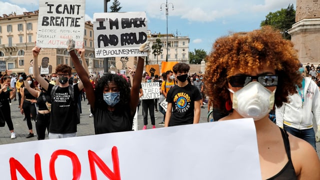 Demonstranten mit Gesichtsmasken halten Plakate in der Höhe. Demonstranten mit Gesichtsmasken halten Plakate in der Höhe.