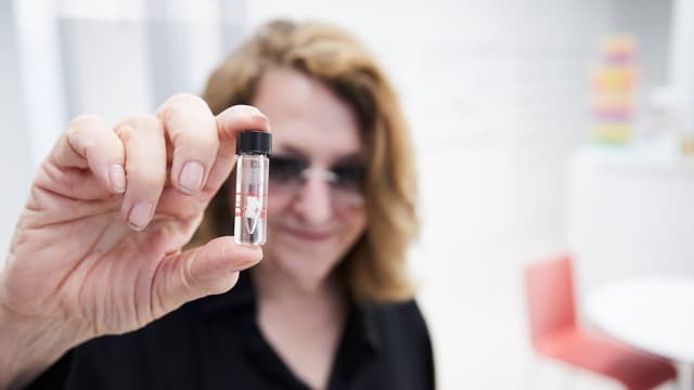 Eine Frau hält ein kleines REagenzglas in der Hand. Eine Frau hält ein kleines REagenzglas in der Hand.