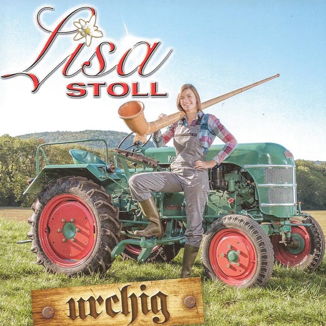 Stoll steht mit Alphorn vor Traktor auf Wiese. Stoll steht mit Alphorn vor Traktor auf Wiese.