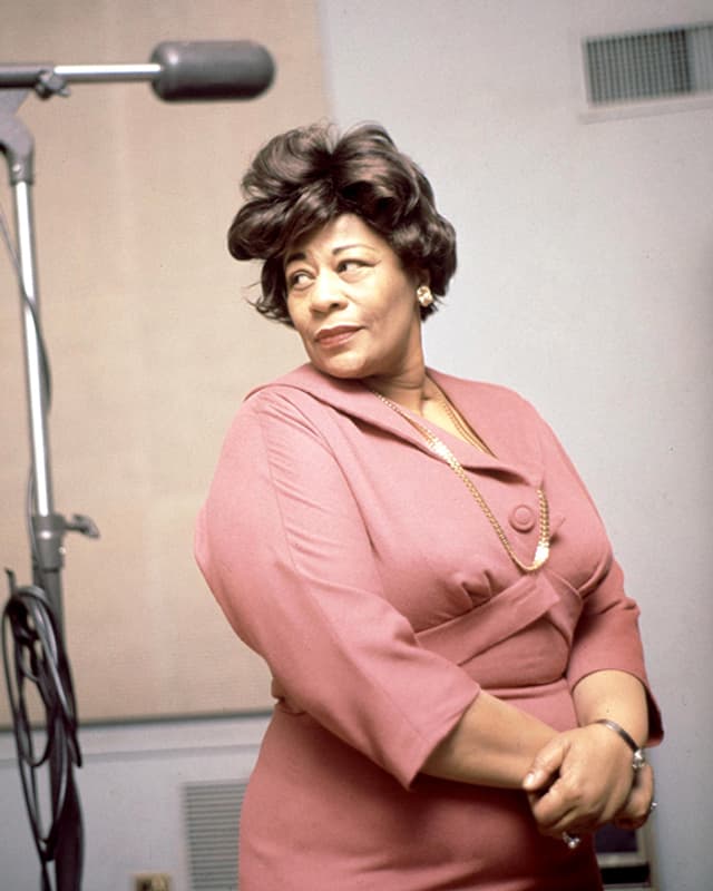 Ella Fitzgerald steht neben einem Mikrophon. Ella Fitzgerald steht neben einem Mikrophon.