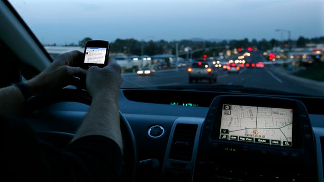 Jemand bedient ein Smartphone während des Fahrens, das Navigationsgerät leuchtet in der Dämmerung. Jemand bedient ein Smartphone während des Fahrens, das Navigationsgerät leuchtet in der Dämmerung.