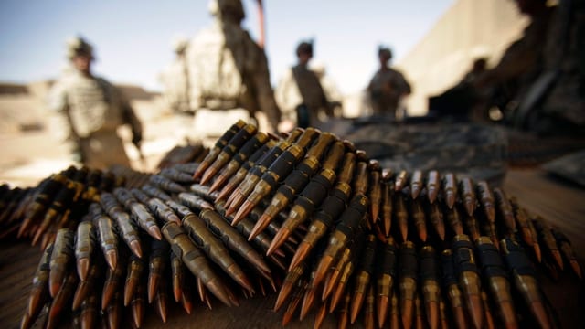 Munition liegt im Vordergrund auf einem Tisch, im Hintergrund vier amerikanische Soldaten mit Helm. Munition liegt im Vordergrund auf einem Tisch, im Hintergrund vier amerikanische Soldaten mit Helm.