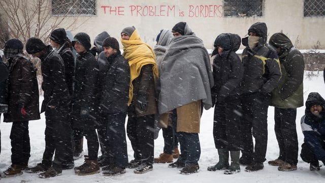 Männer stehen in einer Reihe im Schneetreiben, einige sind mit Wolldecken vermummt. Männer stehen in einer Reihe im Schneetreiben, einige sind mit Wolldecken vermummt.