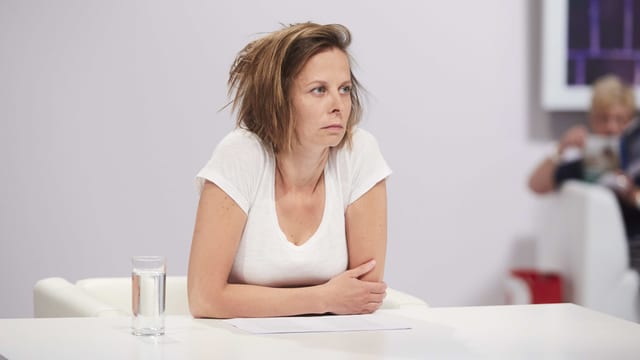 Eine Frau sitzt aufgestützt an einem Tisch und hört jemandem zu. Eine Frau sitzt aufgestützt an einem Tisch und hört jemandem zu.