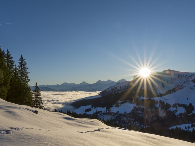Die Sonne geht am wolkenlosen Himmel an einer Bergkrete auf.