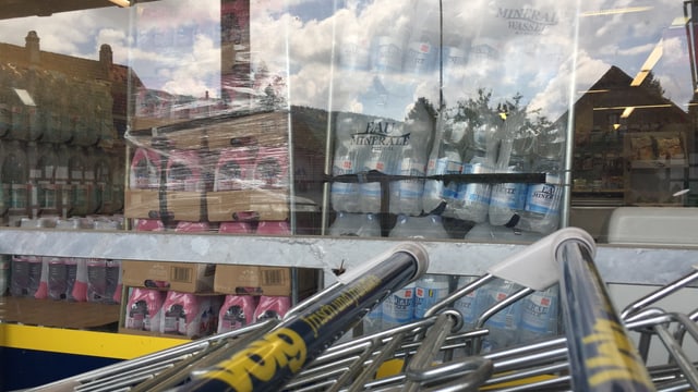 Wasserflaschen hinter einem Schaufenster, davor Postiwägeli Wasserflaschen hinter einem Schaufenster, davor Postiwägeli
