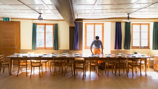 Ein grosses Esszimmer in einem Asylbewerberheim, ein Mann deckt den Tisch um den viele Stühe bereit stehen. Ein grosses Esszimmer in einem Asylbewerberheim, ein Mann deckt den Tisch um den viele Stühe bereit stehen.