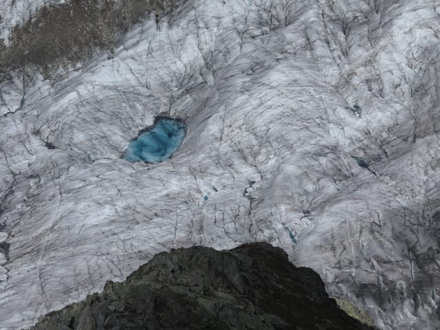 Aufnahme von oben auf einen Gletscher mit einem kleinen blauen Seelein.