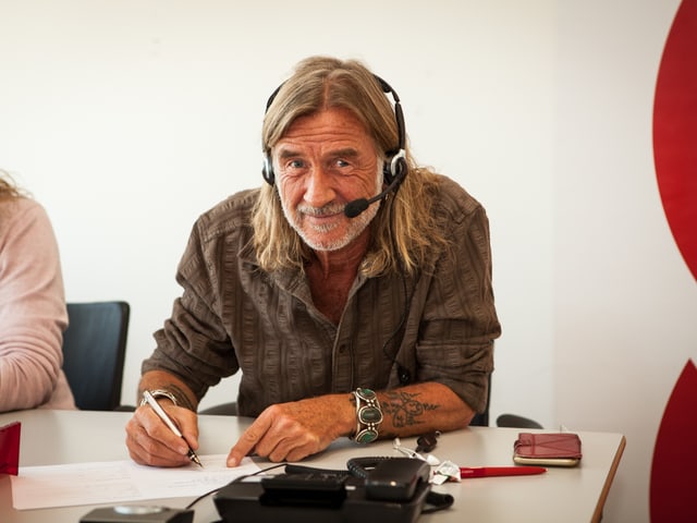 Mann mit langen Haaren und Tattoos am Telefon.