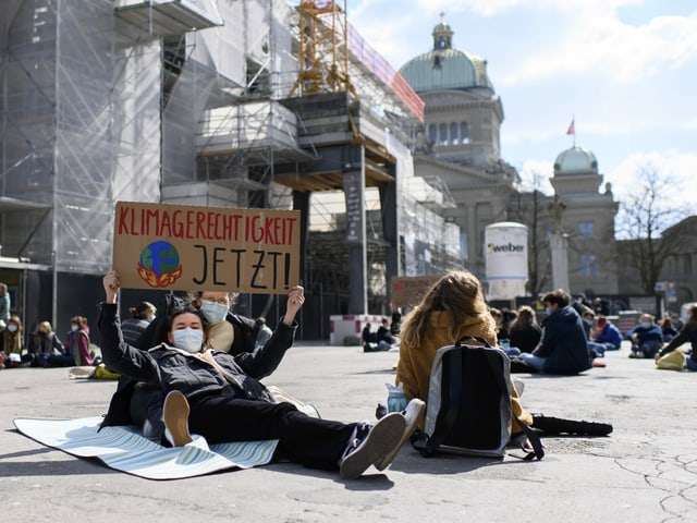 Demonstrierender liegt am Boden und hält Schild hoch. Darauf steht: Klimagerechtigkeit jetzt.