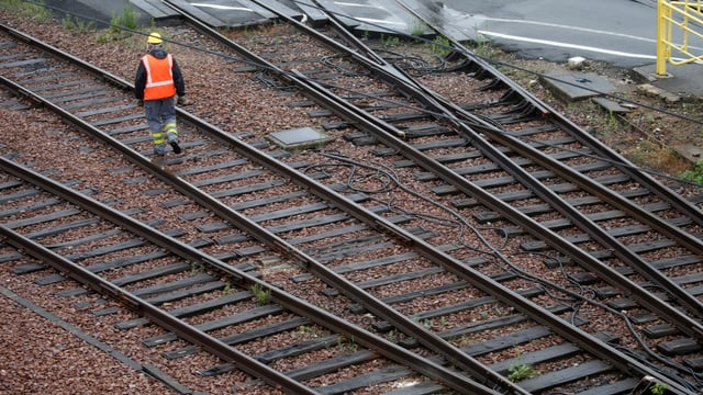Ein Arbeiter mit Leuchtweste geht auf einem Bahngleis. Ein Arbeiter mit Leuchtweste geht auf einem Bahngleis.