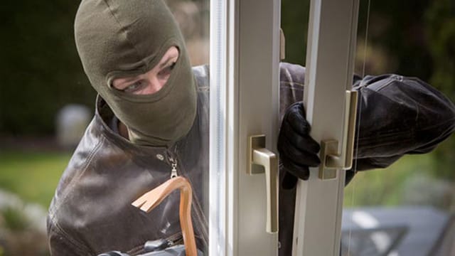 Eine maskierte Person bricht ein Fenster auf. Eine maskierte Person bricht ein Fenster auf.