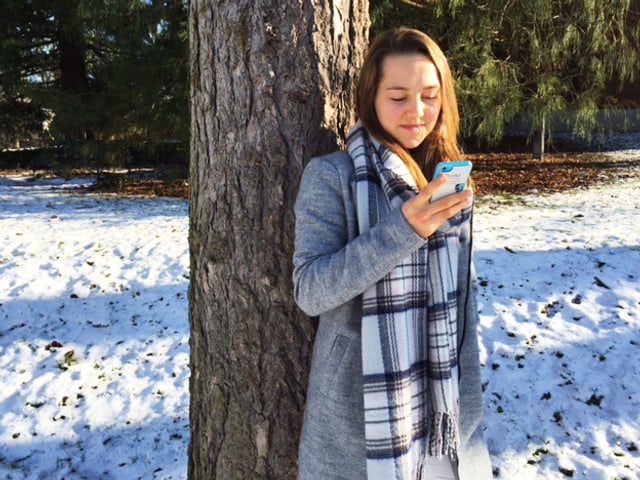 Ein Mädchen lehnt an einem Baum, ein Smartphone in der Hand. Ein Mädchen lehnt an einem Baum, ein Smartphone in der Hand.