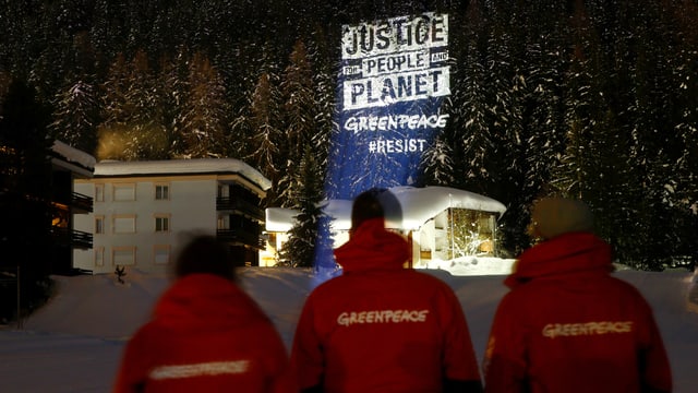 Drei Aktivisten schauen auf Projektion. Es steht: Justice, People, Planet. Drei Aktivisten schauen auf Projektion. Es steht: Justice, People, Planet.