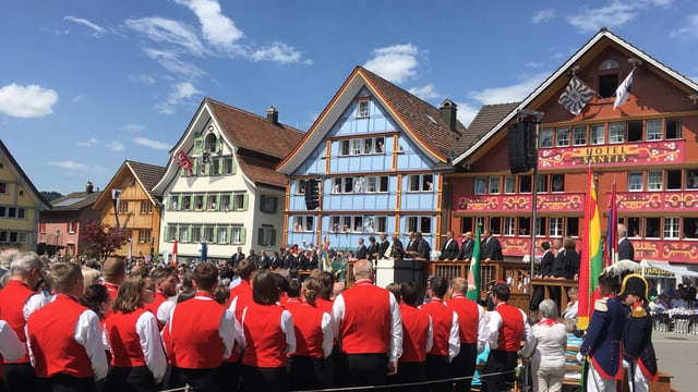 Hintergrund: Bunte Hausfassaden, Vordergrund: Personnen im Ring von hinten fotografiert Hintergrund: Bunte Hausfassaden, Vordergrund: Personnen im Ring von hinten fotografiert