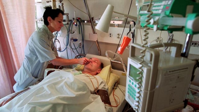 Eine Krankenpflegerin bemüht sich um einen Patienten im Spitalbett.