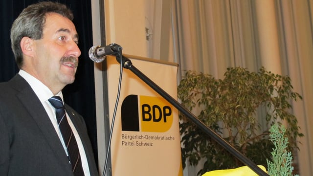 Heinz Siegenthaler steht mit Mikrophon (am Rednerpult), hinter ihm ein Banner der BDP.