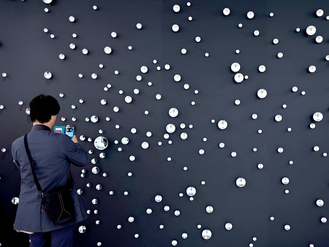 Ein Mann steht mit einem Smartphone vor einem Kunstwerk, das an einen Sternenhimmel erinnert. Ein Mann steht mit einem Smartphone vor einem Kunstwerk, das an einen Sternenhimmel erinnert.