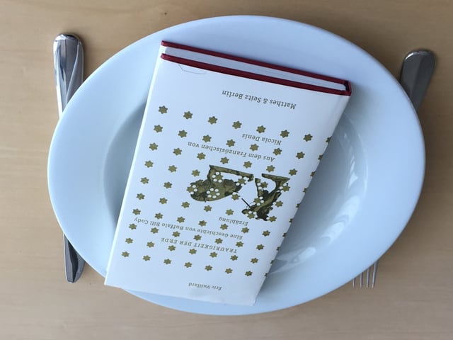 Das Buch «Traurigkeit der Erde» von Éric Vuillard liegt auf einem weissen Teller. Messer und Gabel liegt daneben. Das Buch «Traurigkeit der Erde» von Éric Vuillard liegt auf einem weissen Teller. Messer und Gabel liegt daneben.
