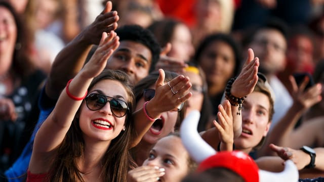 Zu sehen ist eine Menschenpulk. Die Frauen und Männer gucken augenscheinlich einem Fussballspiel an einem Public Viewing zu und verwerfen die Hände. Zu sehen ist eine Menschenpulk. Die Frauen und Männer gucken augenscheinlich einem Fussballspiel an einem Public Viewing zu und verwerfen die Hände.
