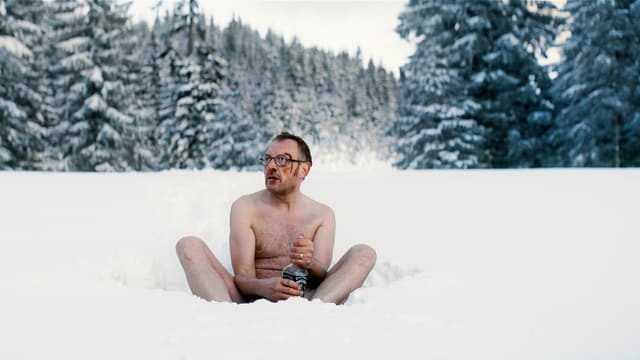 Ein Mann sitzt nackt im Schnee und hält eine Flasche.