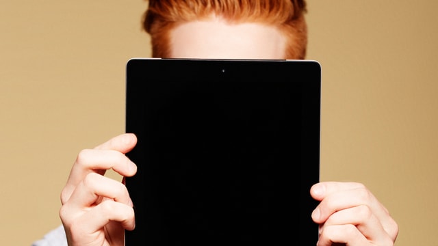 Ein Mann mit rotem Haar versteckt sich hinter einem Tablet.