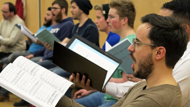 Ein Chor bei der Probe: Männer mit einem Notenblatt in der Hand singen. Ein Chor bei der Probe: Männer mit einem Notenblatt in der Hand singen.