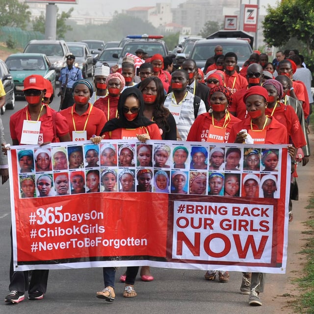 Demonstranten mit roten Kleidern und Mundschutzen tragen ein Transparent mit Bildern der vermissten Mädchen und der Aufschrift: «Bringt unsere Mädchen zurück - jetzt».
