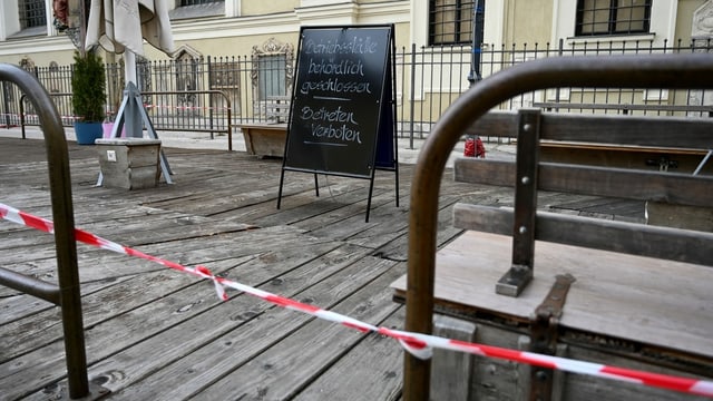 Eine abgesperrte Holz-Terrasse. Darauf stehen ein Schild und einzelne Gartenmöbel. Eine abgesperrte Holz-Terrasse. Darauf stehen ein Schild und einzelne Gartenmöbel.