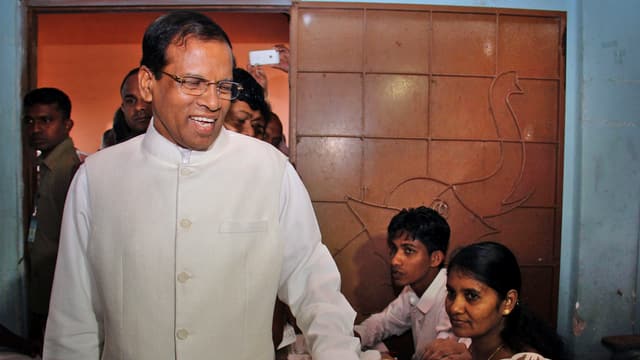 Sirisena (mit Brille) lächelt stehend im Wahlbüro. Sirisena (mit Brille) lächelt stehend im Wahlbüro.