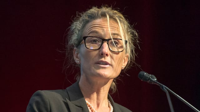 Eine blonde Frau mit Brille spricht in ein Mikrofon. Eine blonde Frau mit Brille spricht in ein Mikrofon.