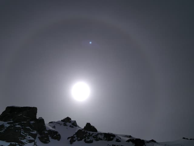 Bergfelsen und darüber Sonne mit hellem Ring darum herum.