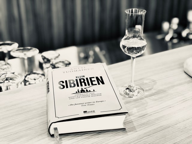 «Klein-Sibirien» von Antti Tuomainen liegt auf einem Tresen. Daneben steht ein Glas mit Schnaps. «Klein-Sibirien» von Antti Tuomainen liegt auf einem Tresen. Daneben steht ein Glas mit Schnaps.