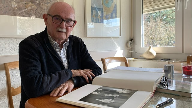 Älterer Mann mit Brille sitzt an Tisch, hat Fotobuch vor sich. Älterer Mann mit Brille sitzt an Tisch, hat Fotobuch vor sich.