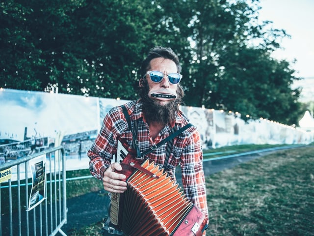 Mann mit Mundharmonika im Mund und Handorgel.