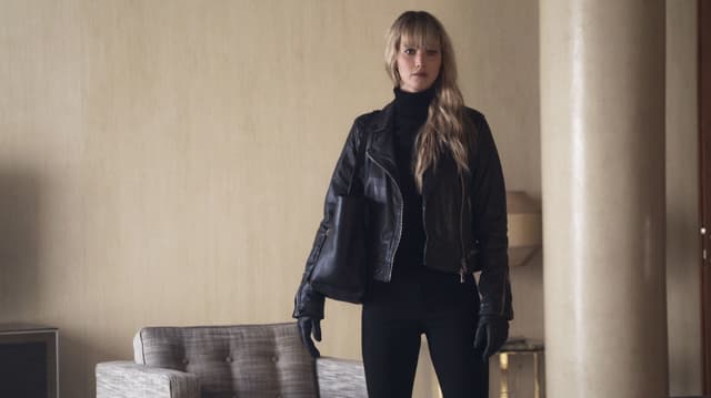 Ein Raum mit einem Sessel, recht im Vordergrund eine Säule aus Stein. Daneben steht eine junge Frau in Lederjacke, Hose und mit Tasche. Sie hat lange Haare und schaut ernst. Ein Raum mit einem Sessel, recht im Vordergrund eine Säule aus Stein. Daneben steht eine junge Frau in Lederjacke, Hose und mit Tasche. Sie hat lange Haare und schaut ernst.