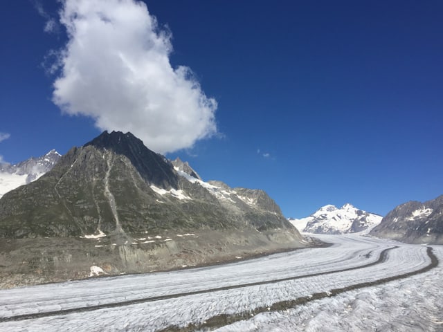 Im Vordergrund Gletschter, dahinter Berge und blauer Himmel. Über einem Berge steht eine Quellwolke.